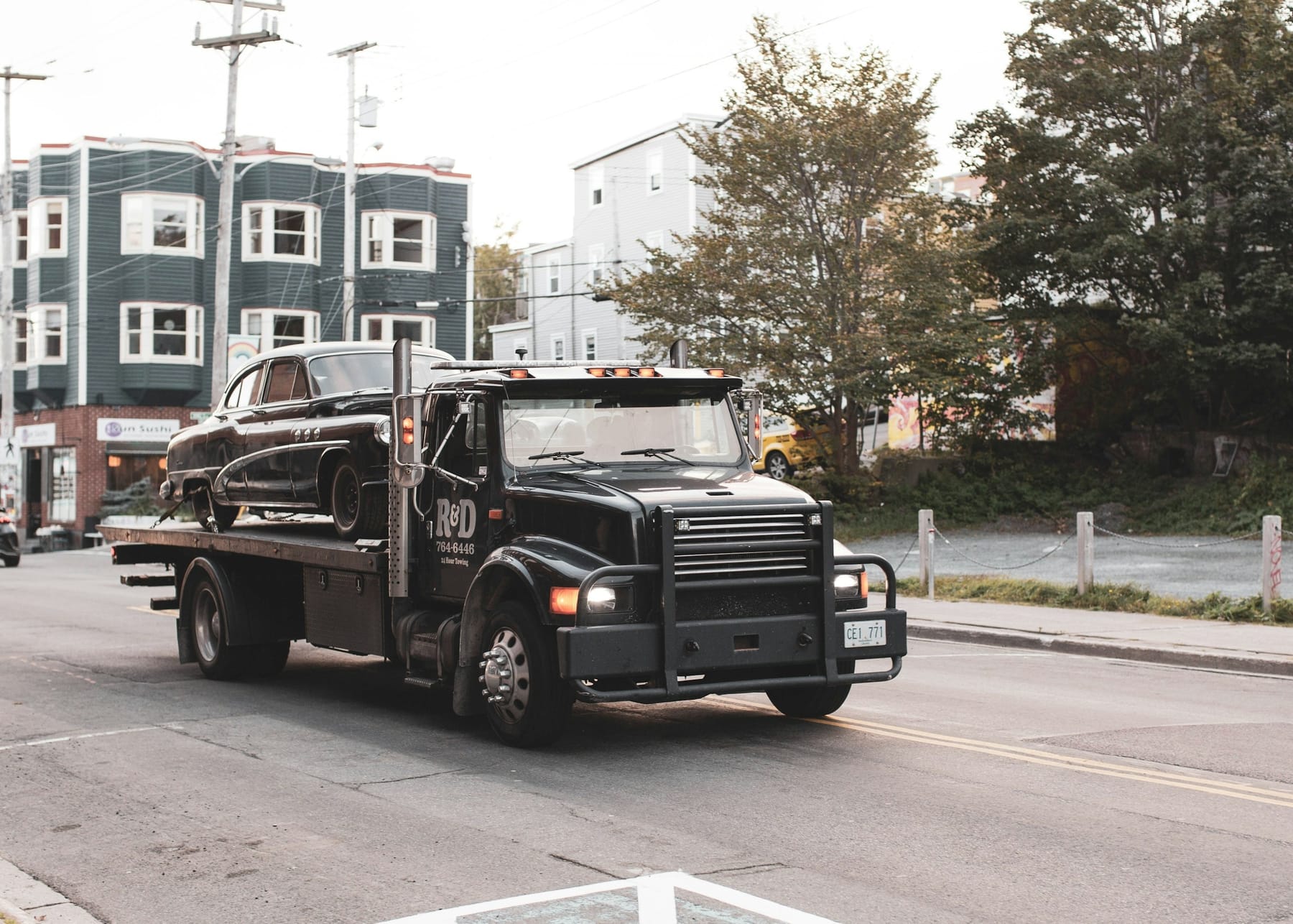 A black flatbed tow truck on an ordinary street in daylight, with a car loaded on the deck.