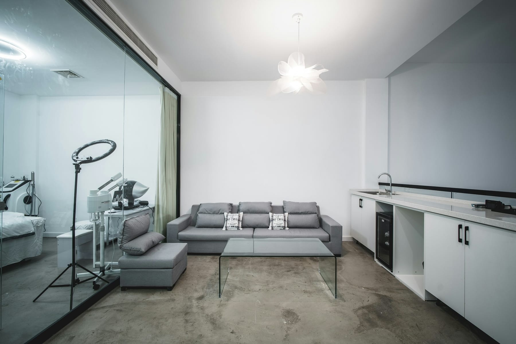 A clinic waiting area with a grey sofa, concrete floor, and a treatment room visible through glass.