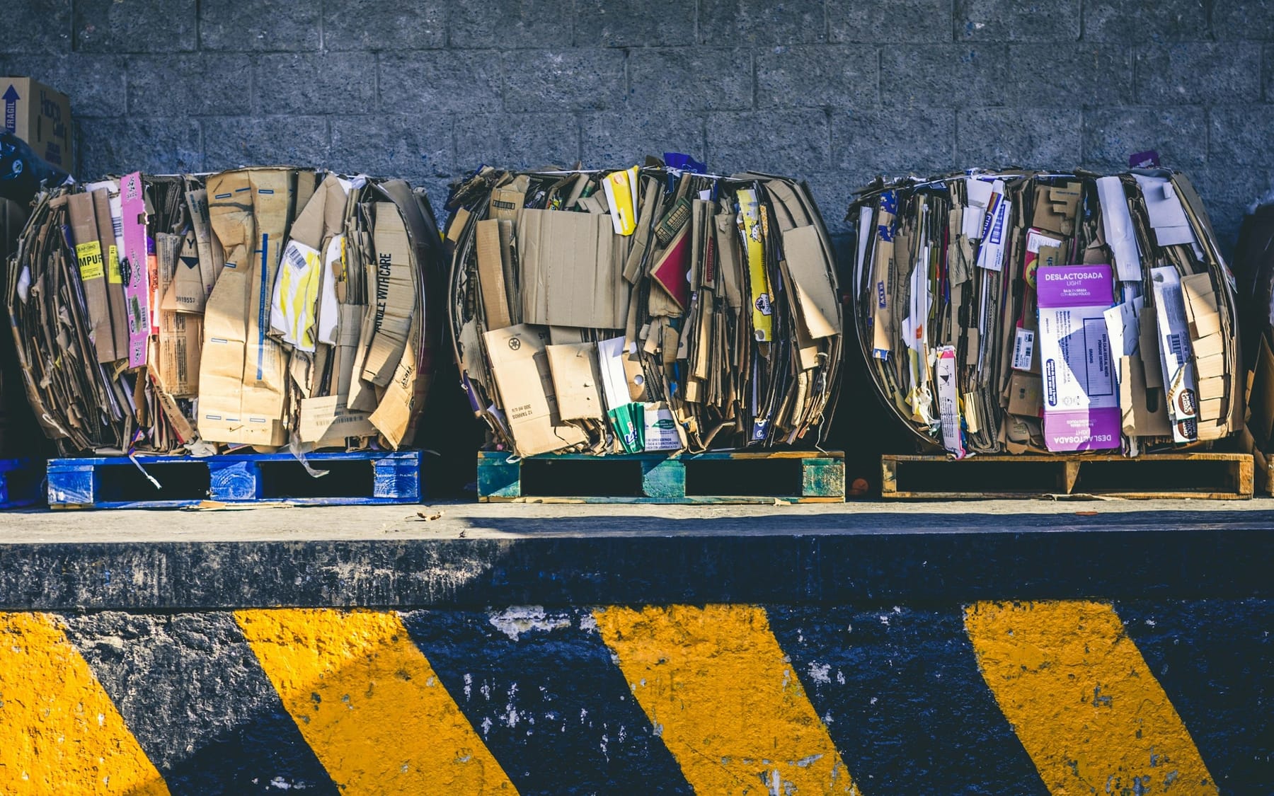 Three baled bundles of flattened cardboard lined up against a wall on a loading dock.