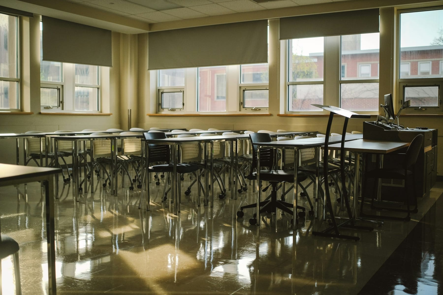An empty classroom with tables, chairs and daylight from a bank of windows.