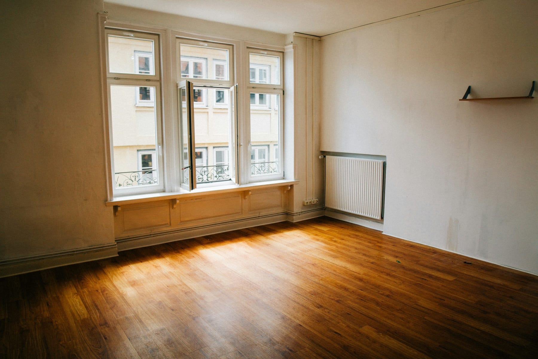 An empty room with a wooden floor and tall windows, nothing left in it.