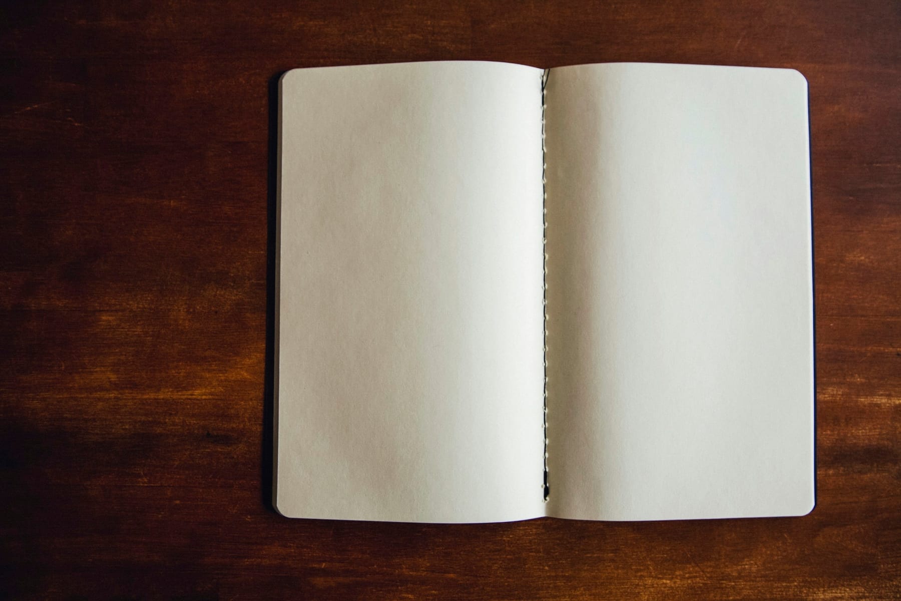 An open blank notebook lying on a dark wooden table.