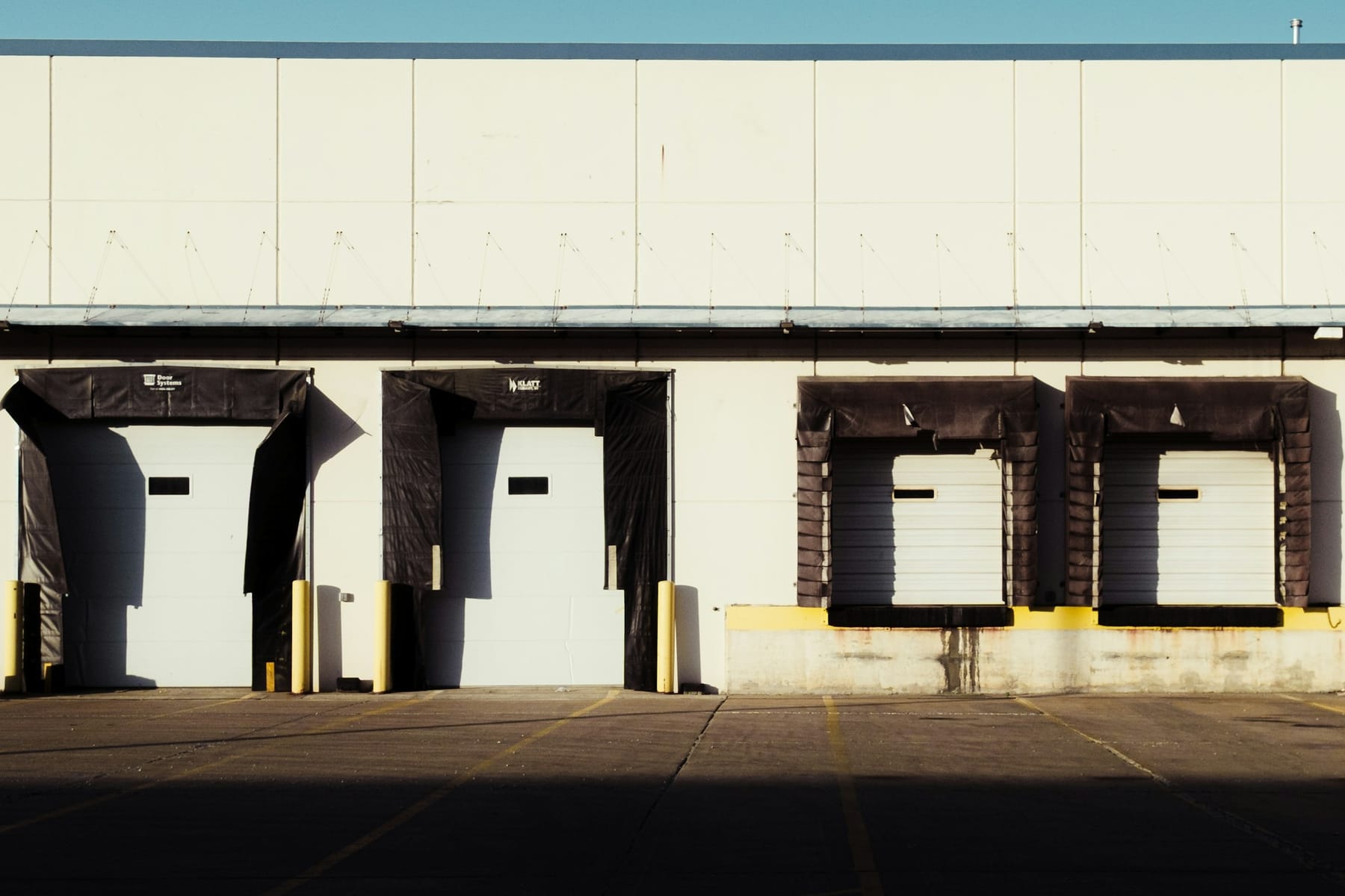 A row of empty loading dock doors on a plain warehouse wall, seen straight on from the yard.