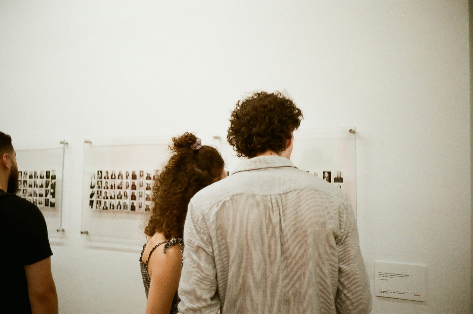Two people standing close to a row of very small works pinned in a line along a white gallery wall.