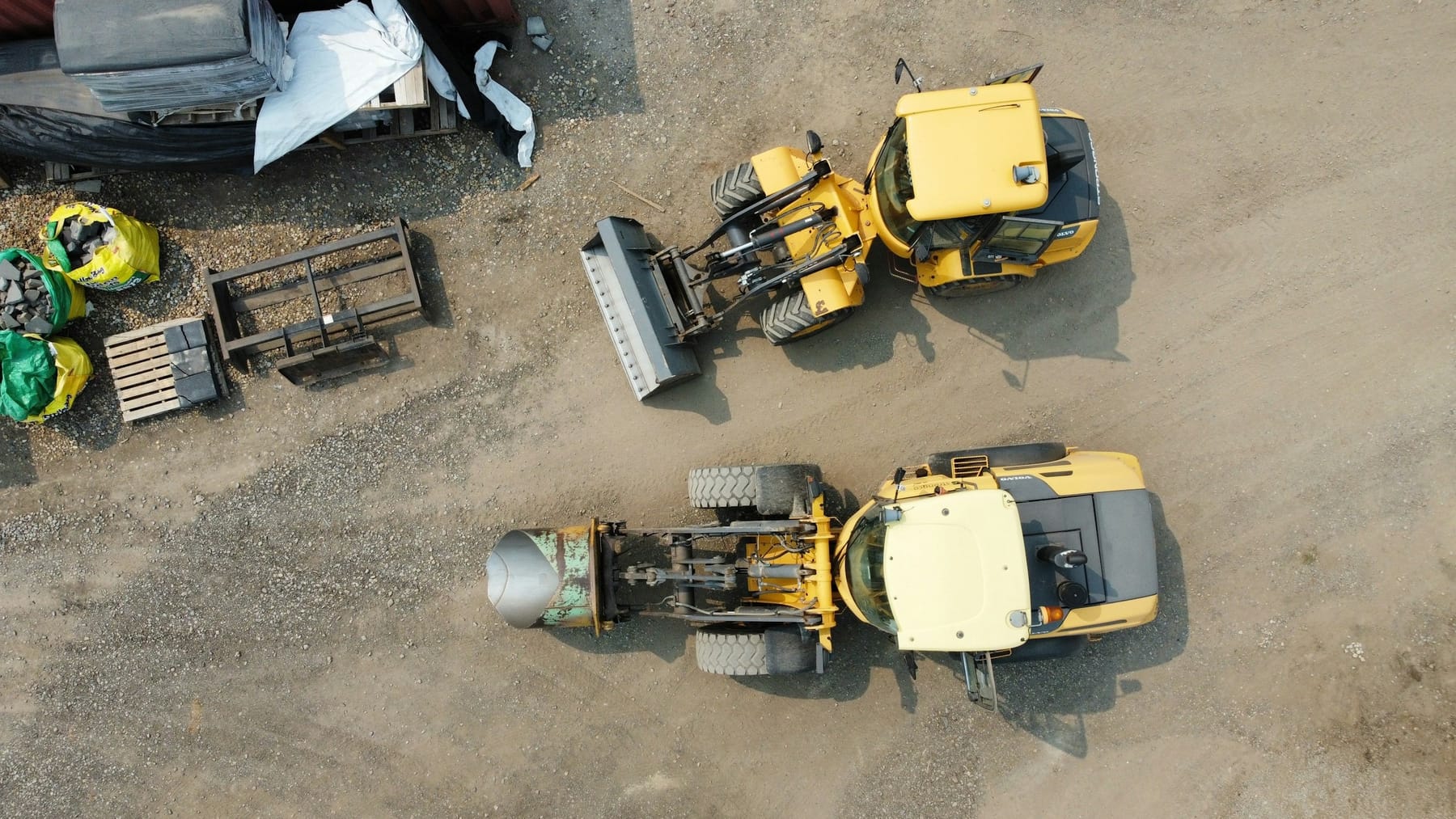 Two wheeled loaders parked on a gravel yard, seen from above in flat daylight.