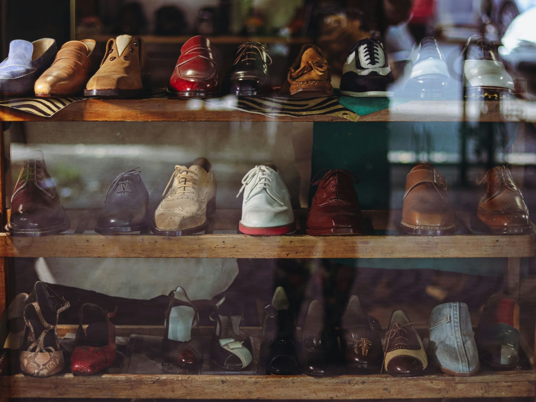 Leather shoes arranged on wooden shelves in a shop window, with shoe trees on the shelf below.