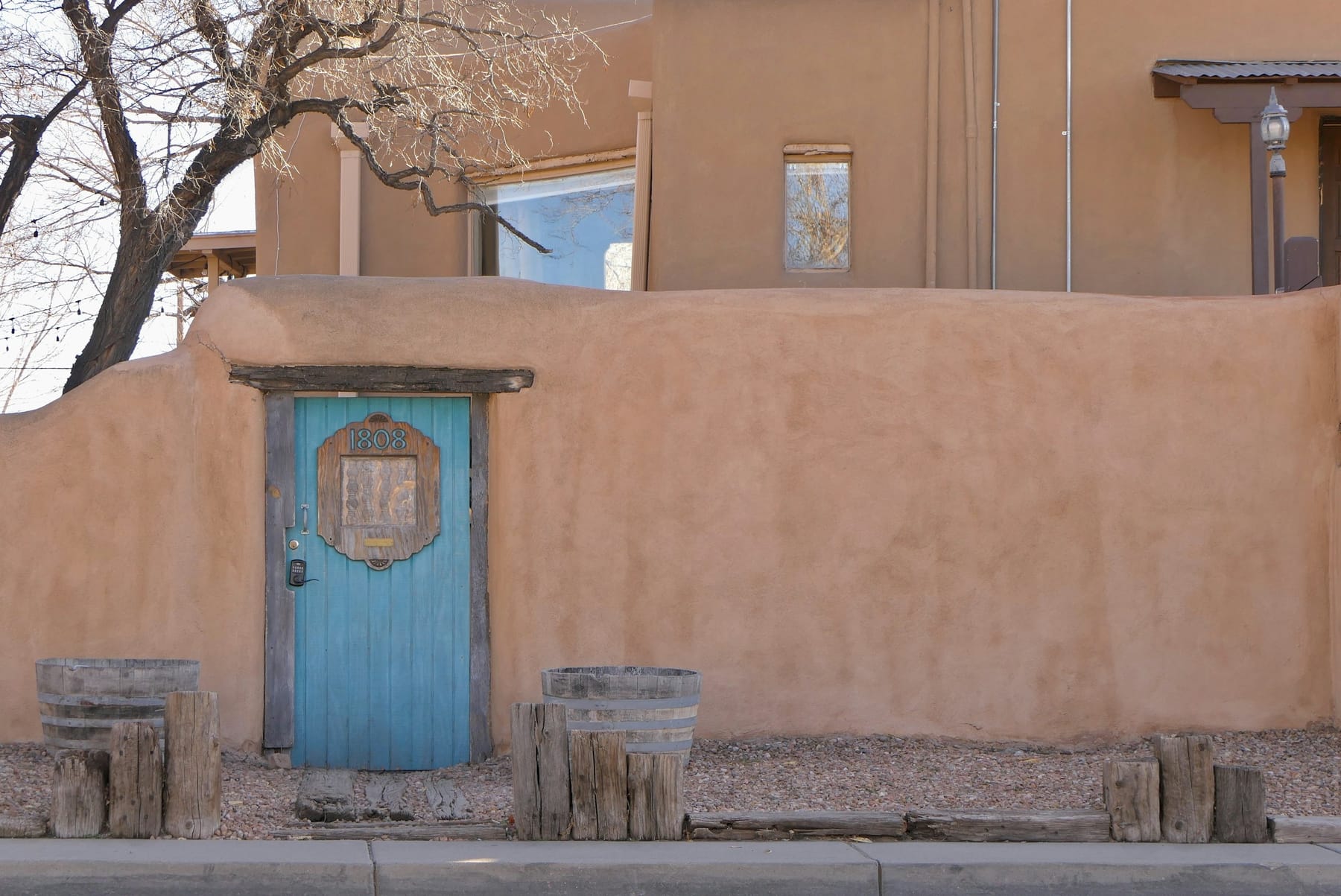 An adobe wall with a blue-painted wooden door and a small window, on a Santa Fe street.