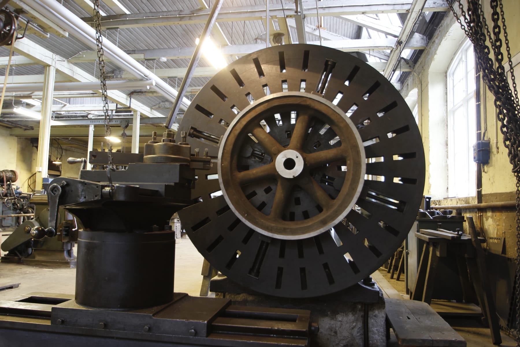 A large flywheel mounted on a lathe faceplate, part-way through a turning operation.