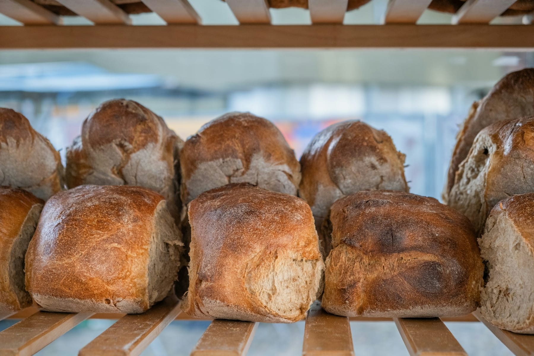 Loaves of bread on a plain wooden shelf in daylight.