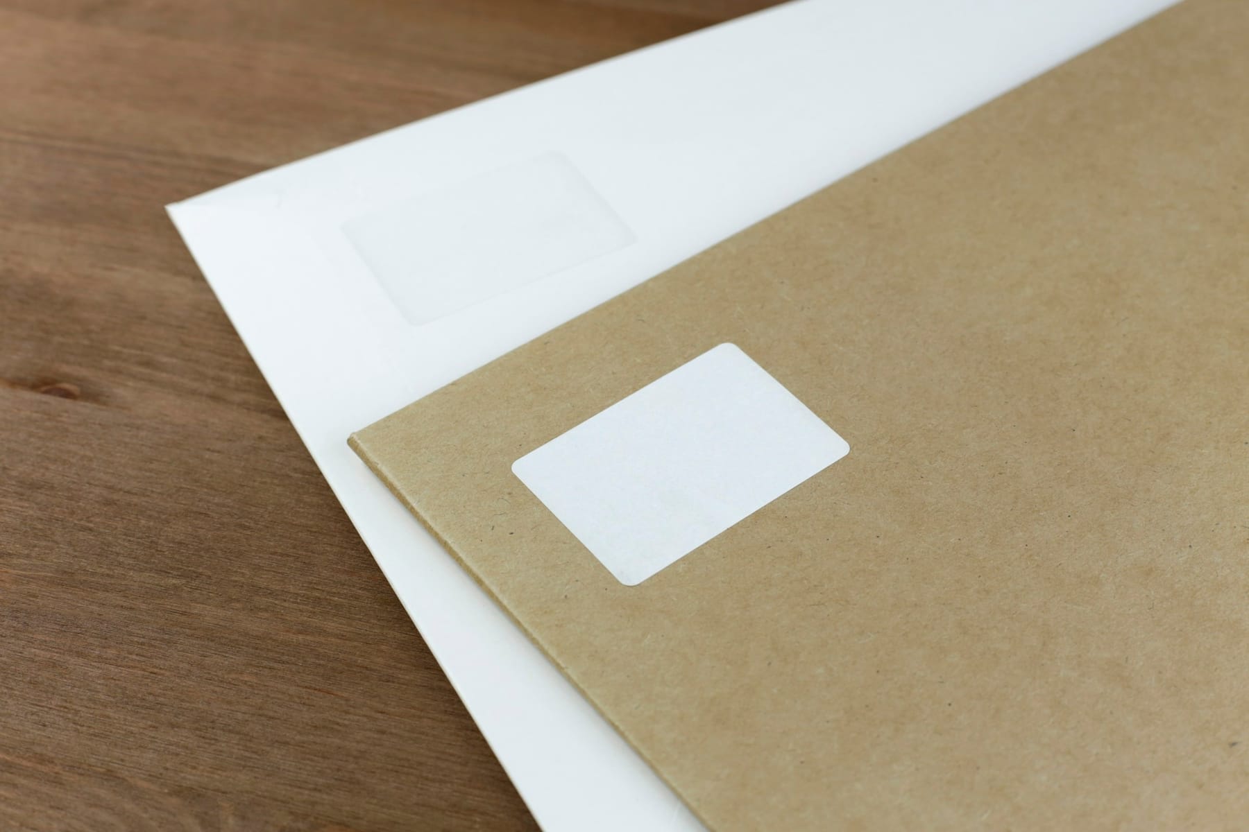 A plain window envelope resting on a sheet of paper on a wooden desk.