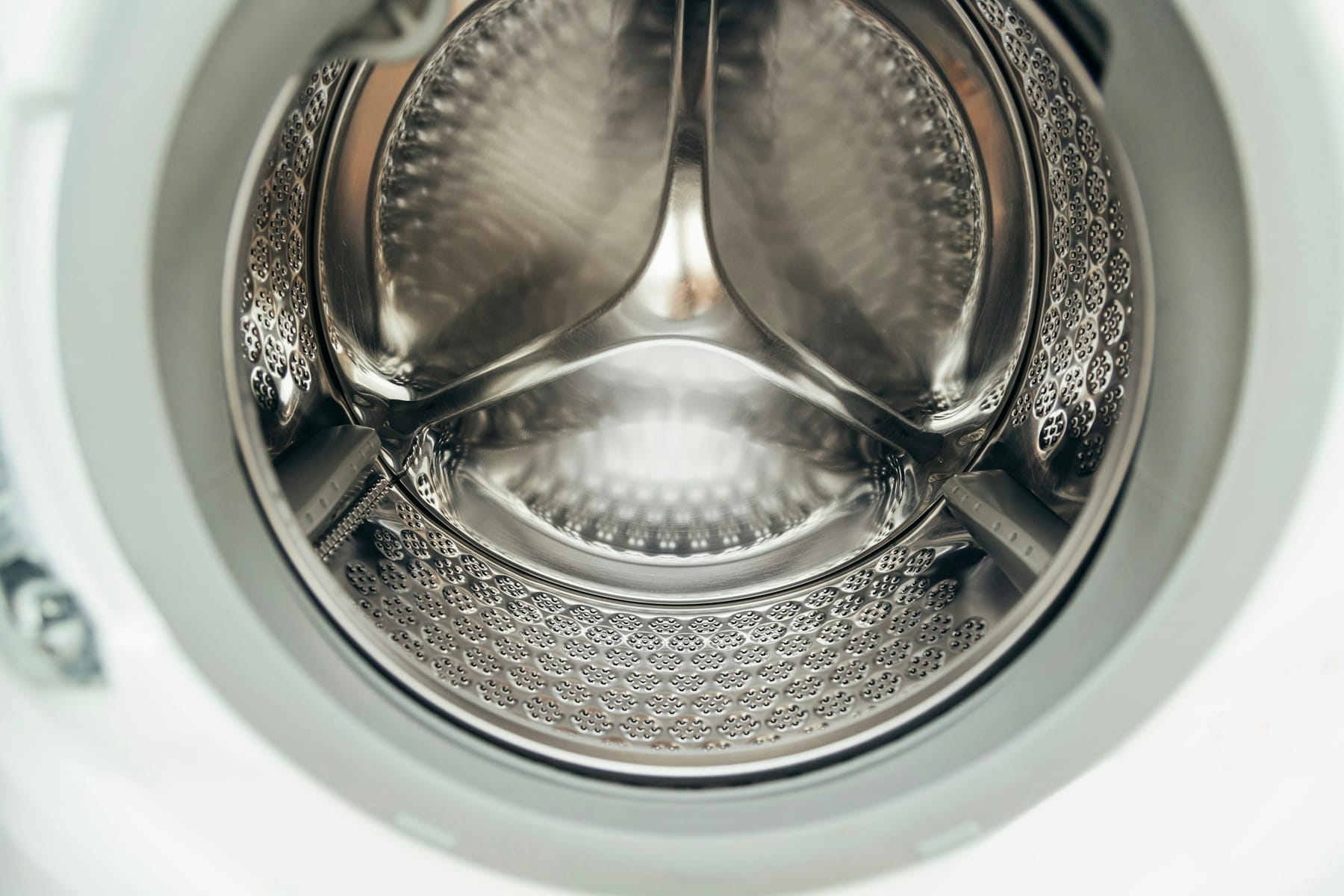 The empty stainless drum of a front-loading washing machine, seen through the door.