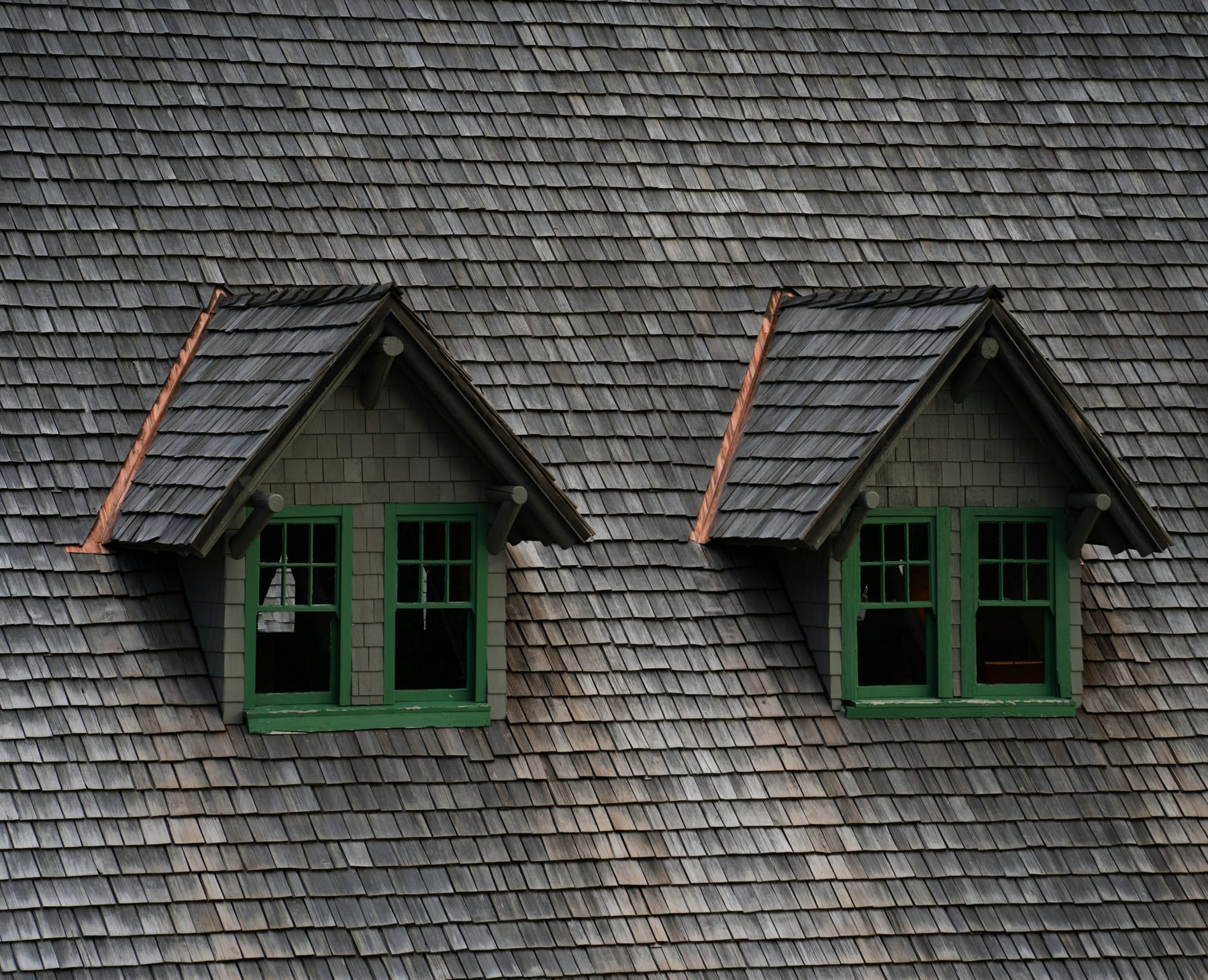 Two dormer windows set into a shingled roof, with copper flashing at each valley.