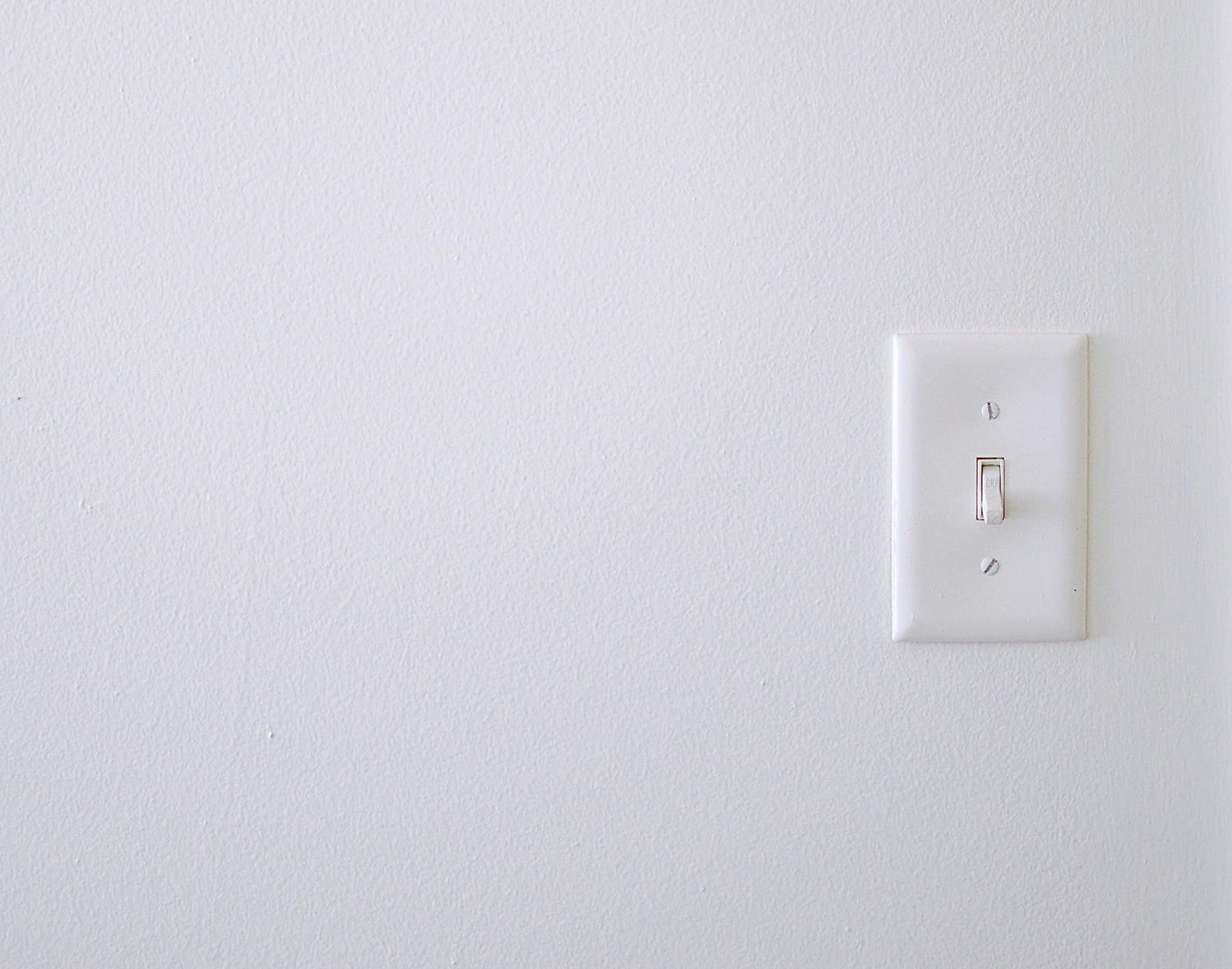 A plain white toggle light switch on a bare white wall.