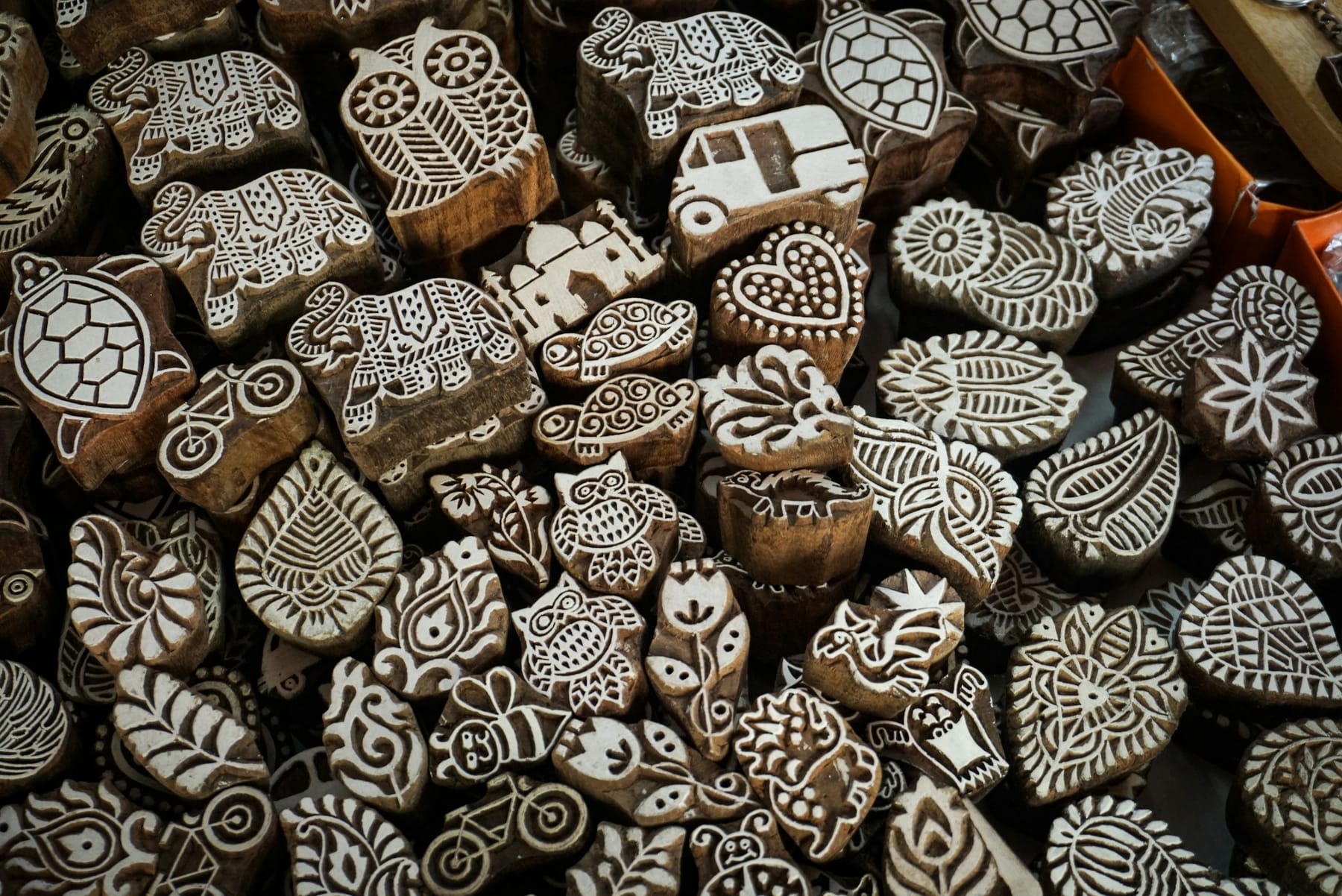 A dense pile of hand-carved wooden printing blocks, each face cut with a different motif — leaves, paisleys, animals and rosettes.